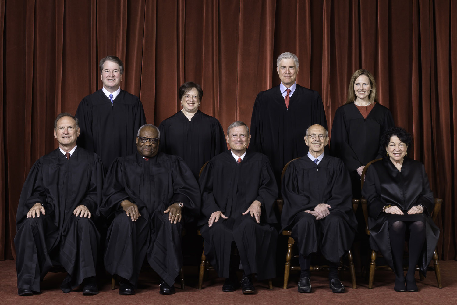 official portrait of nine justices wearing black judicial robes. five justices sit in chairs while four justices stand behind them.