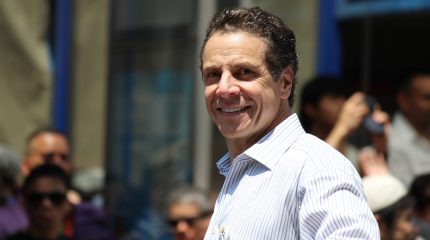andrew cuomo smiling in white button-down shirt with "I love New York" pin