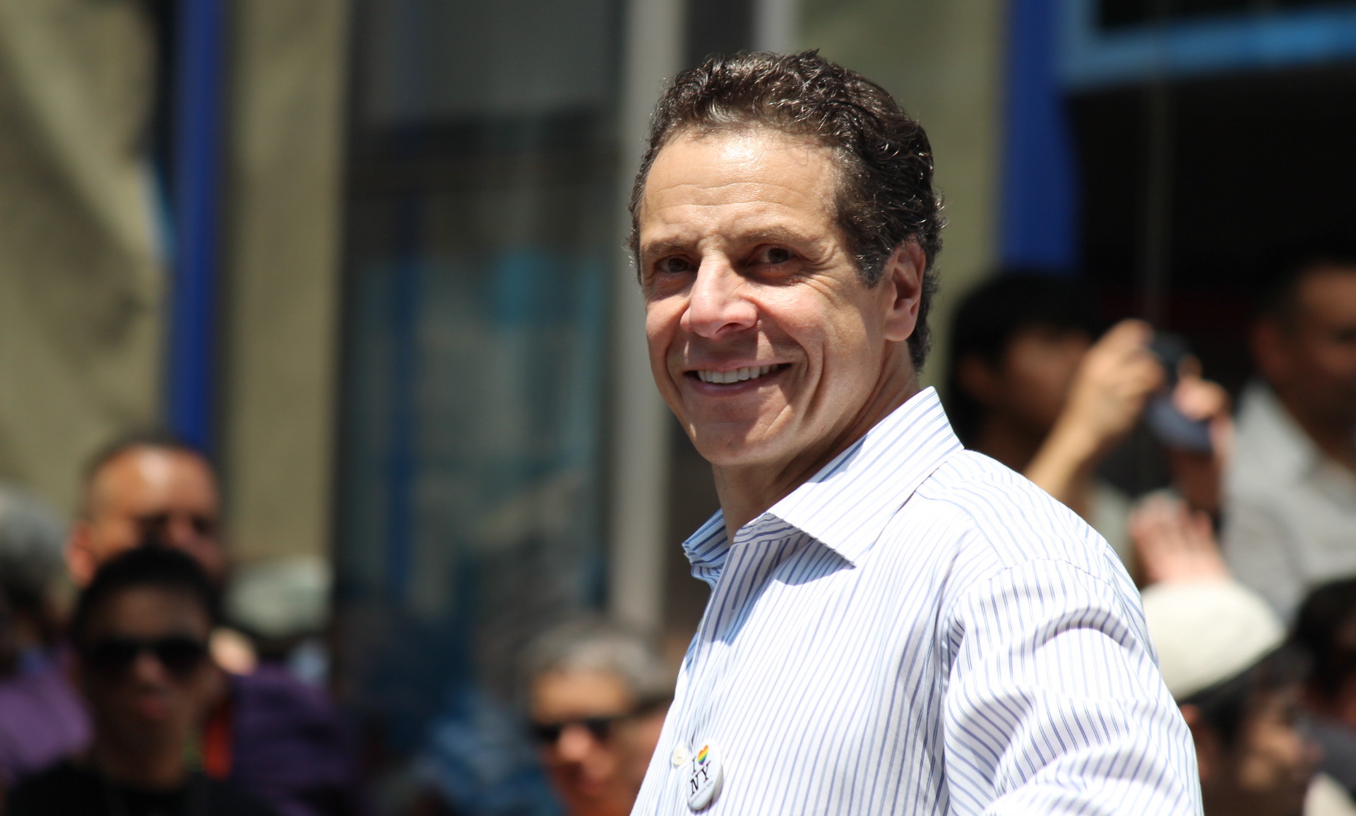 andrew cuomo smiling in white button-down shirt with "I love New York" pin