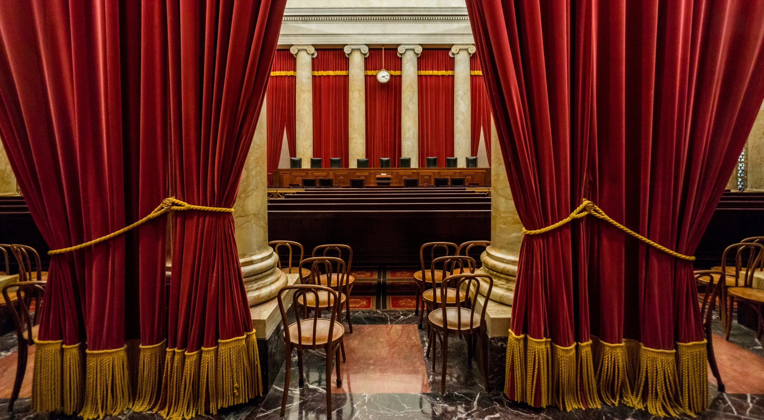 view of empty Supreme Court bench from back of courtroom with large curtains in foreground