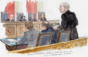 man in dark suit at lectern with two other men sitting at desk and four justices visible in background