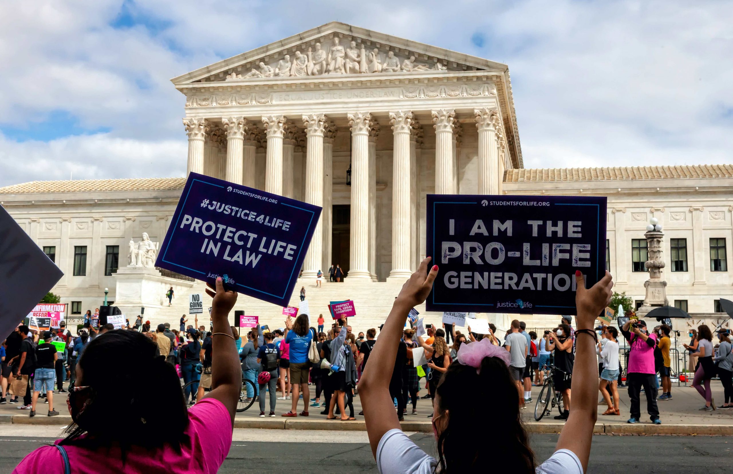 two people with backs to camera holding anti-abortion signs in front of supreme court