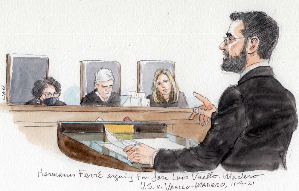 man with beard in dark suit at lectern with right hand pointed; three justices in background