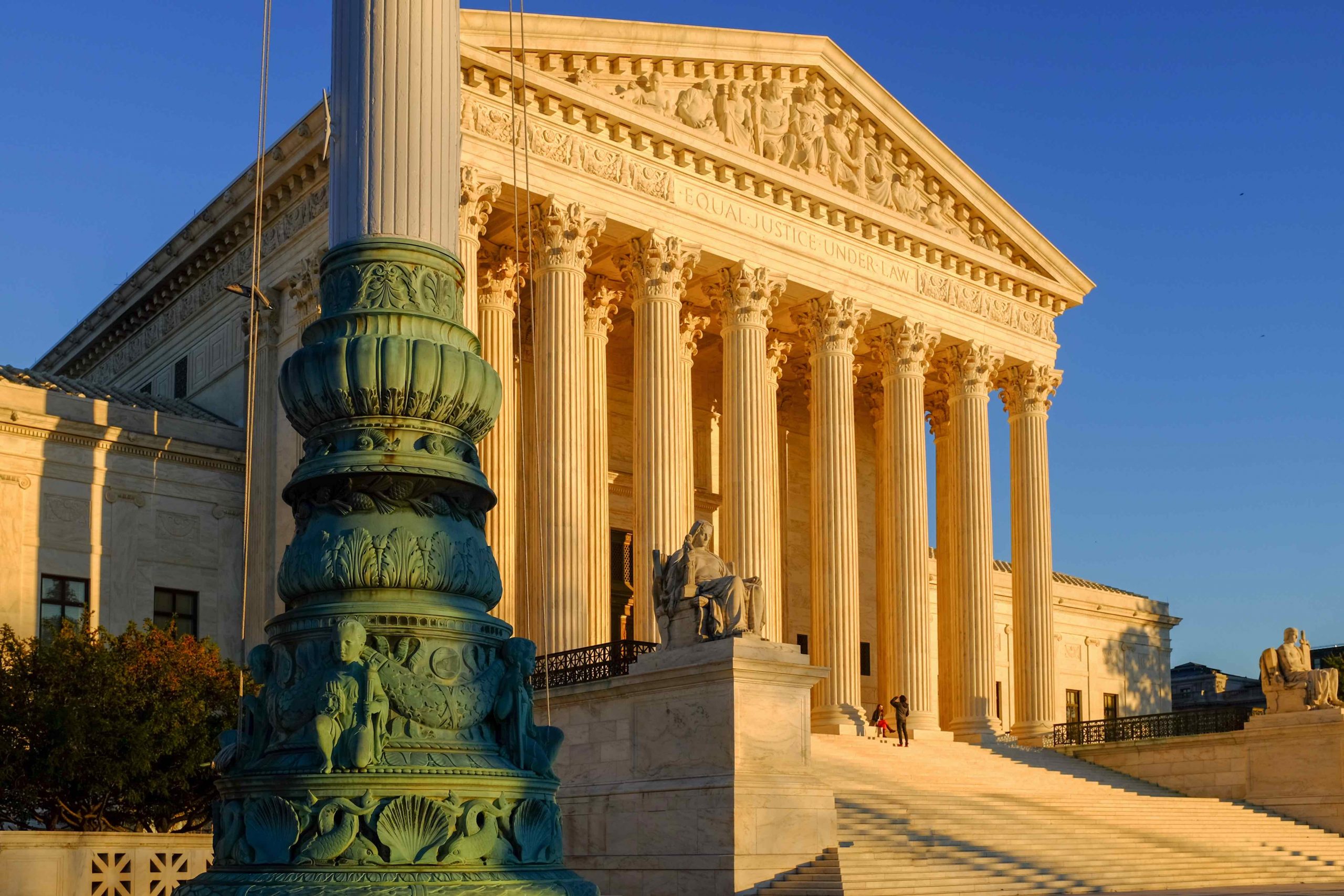 front of supreme court building bathed in golden sunlight with base of flagpole in foreground