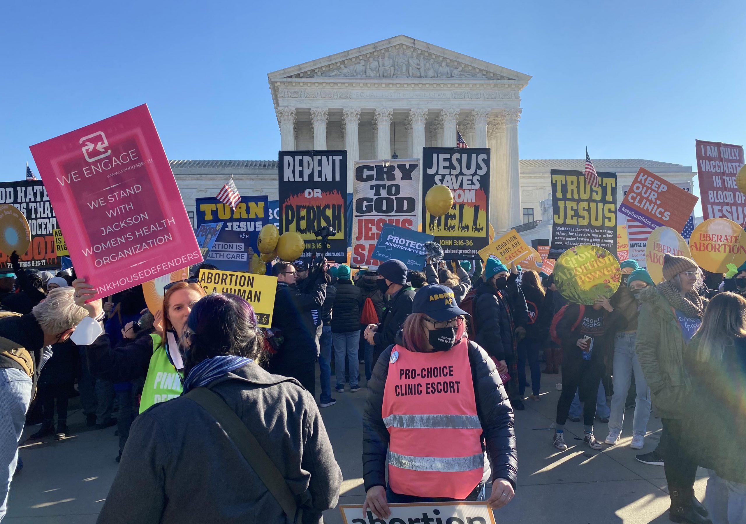 large crowd of supporters and opponents of abortion hold dueling signs in front of supreme court building