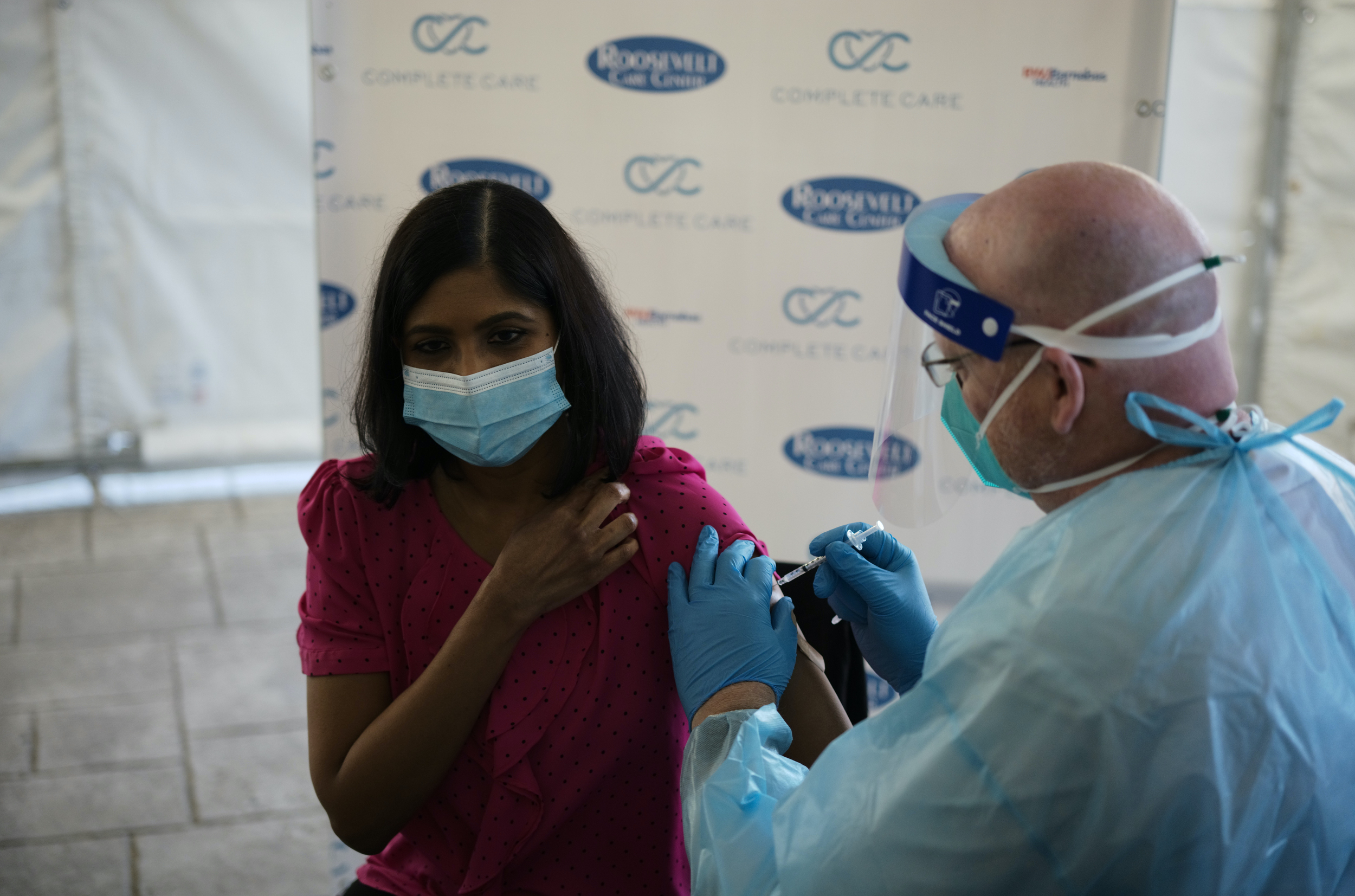 Woman in mask receives covid-19 vaccine from man in mask, hospital smock, and face shield.