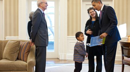 Justice Breyer looks on as president Obama shows a book to a young boy