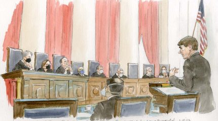 Man speakings at podium in front of eight justices, with six of the justices in masks.