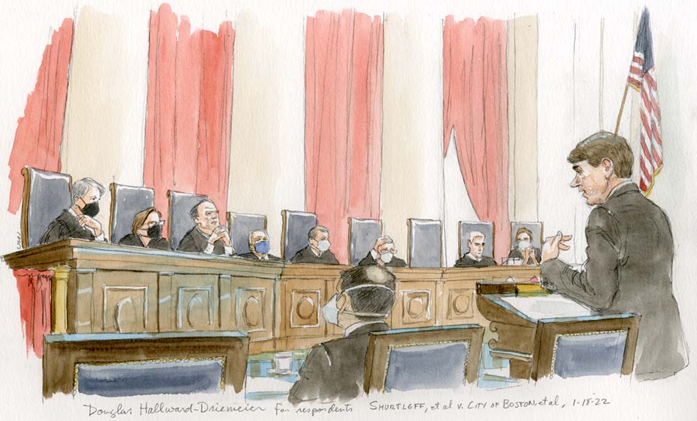 Man speakings at podium in front of eight justices, with six of the justices in masks.