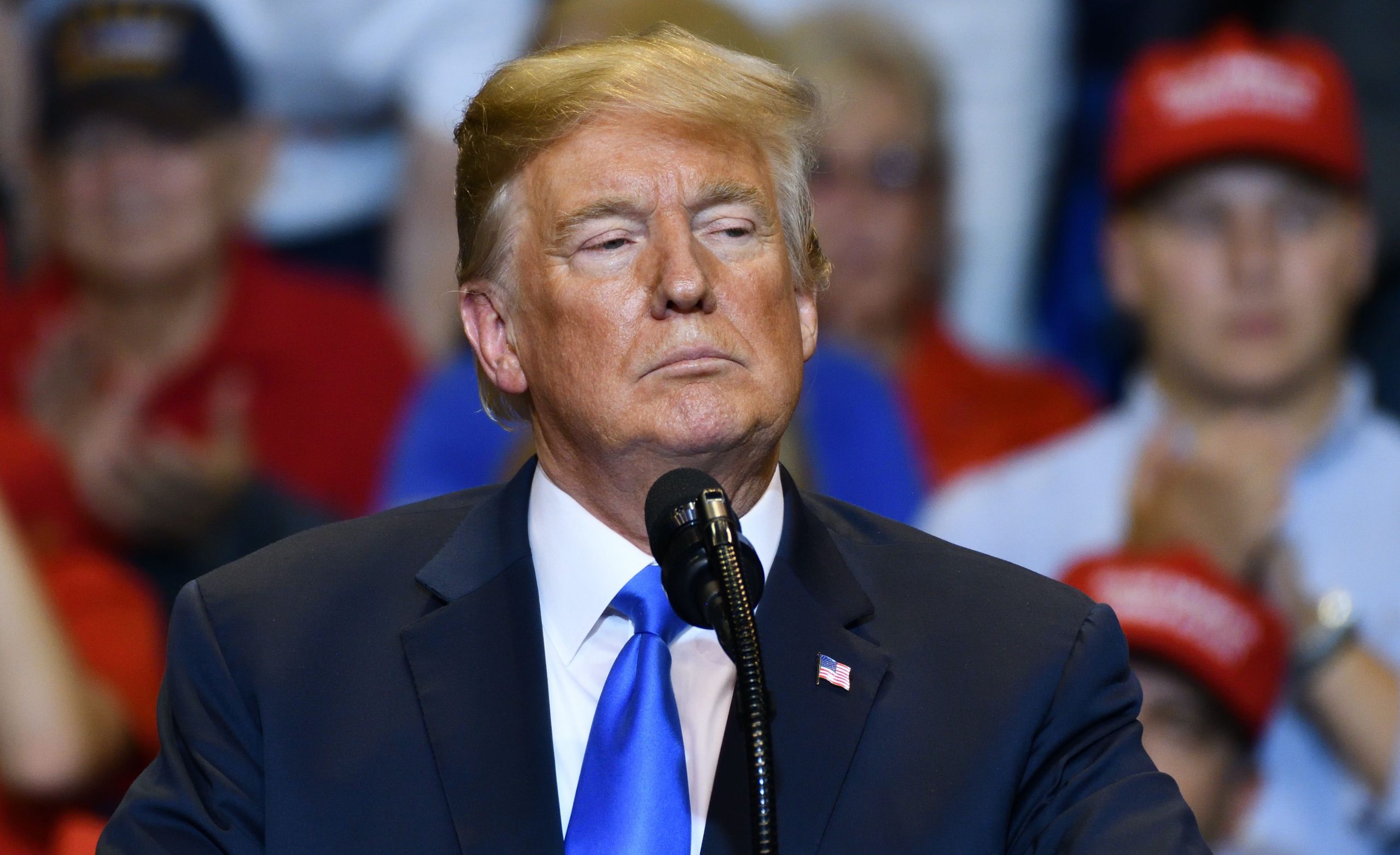 donald trump standing in front of microphone with serious look and crowd of people in background