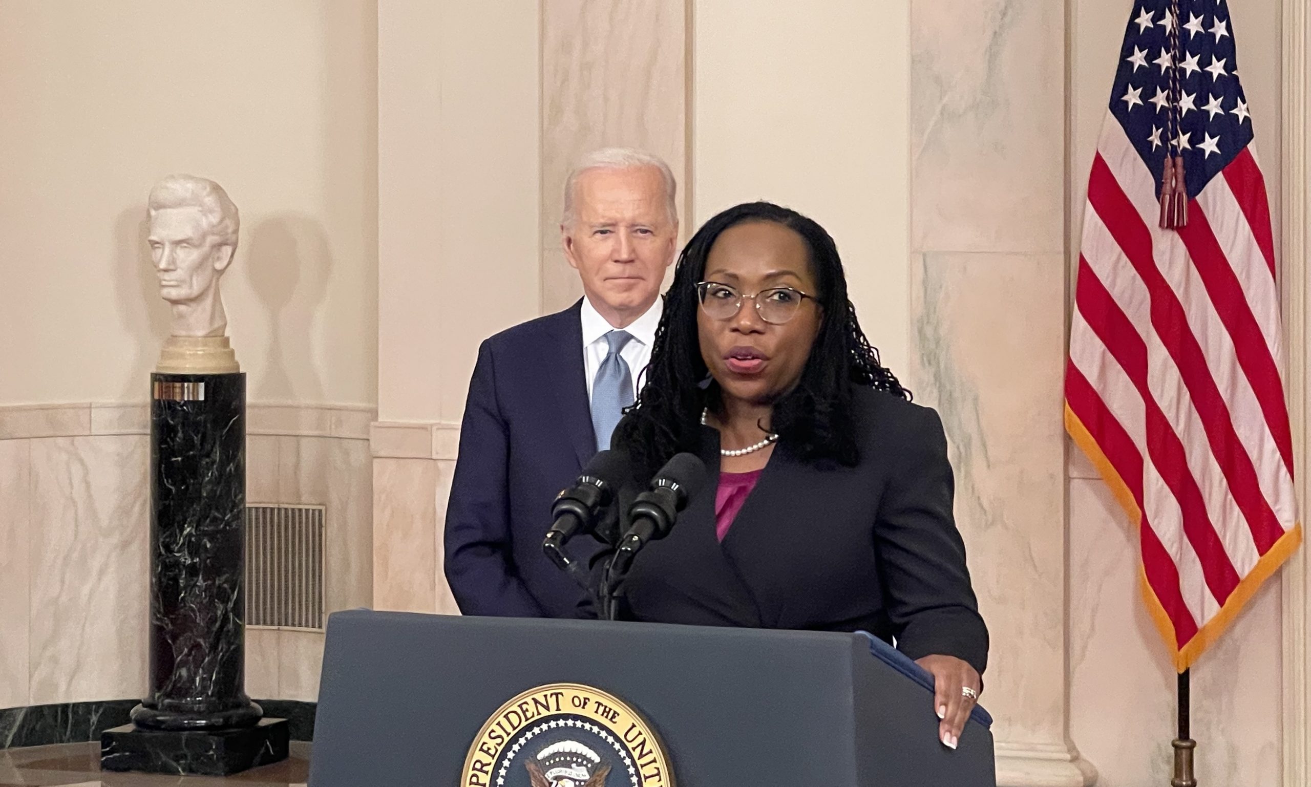 woman speaking at lectern while president stands in background