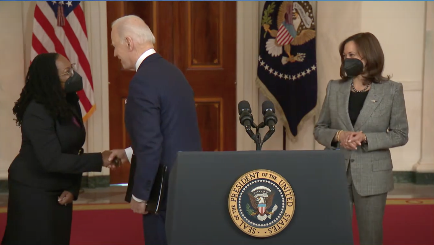 Judge Ketanji Brown Jackson shakes hands with the President, the Vice President watches them.