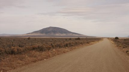 peaceful scene of mountain in distance with gently sloping sides and empty dirt road leading to horizon