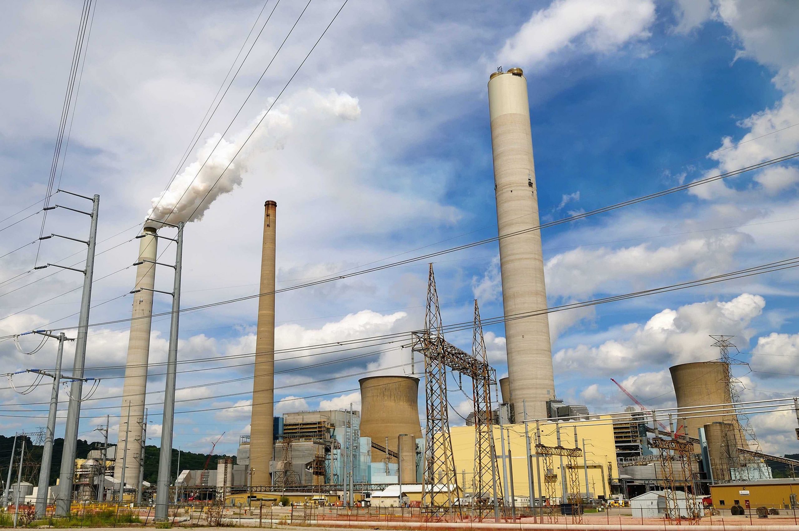 industrial facility with three tall smoke stacks and numerous power lines criss-crossing in foreground