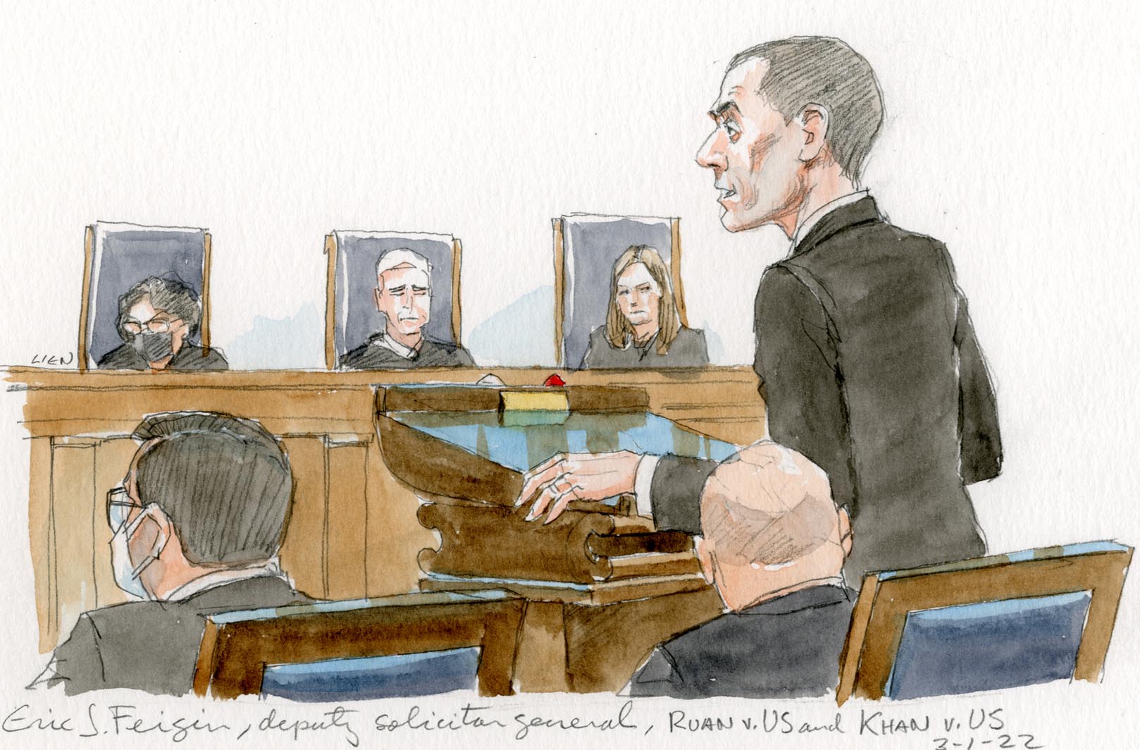 man in dark suit stands at lectern in front of three justices on the bench