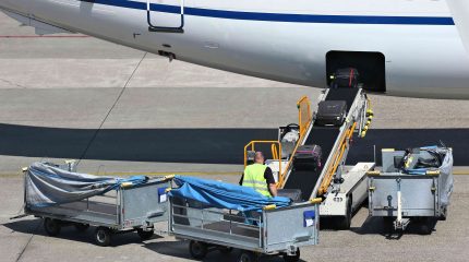 man watches as suitcases move up conveyor belt into the body of airplane