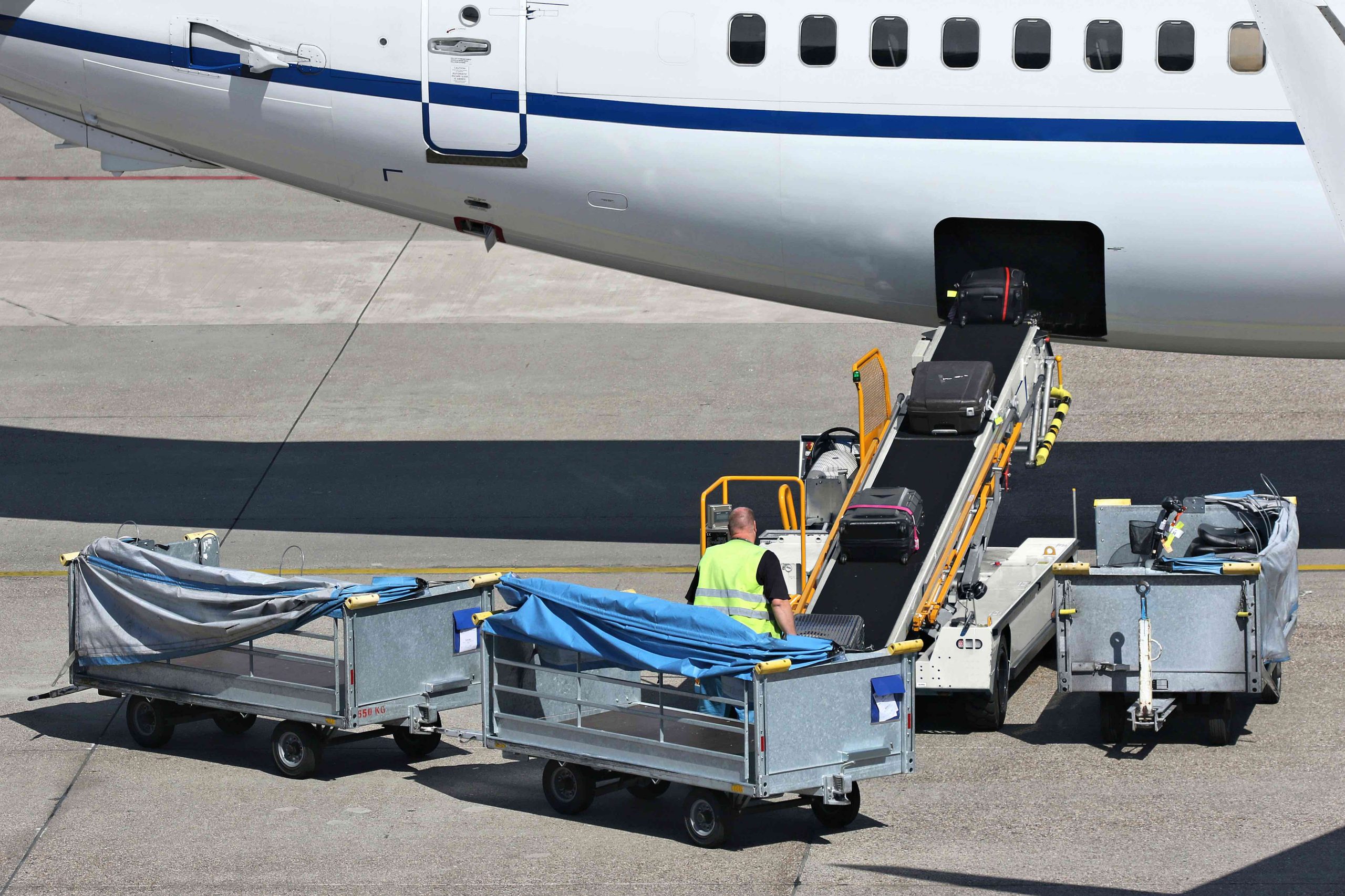 man watches as suitcases move up conveyor belt into the body of airplane