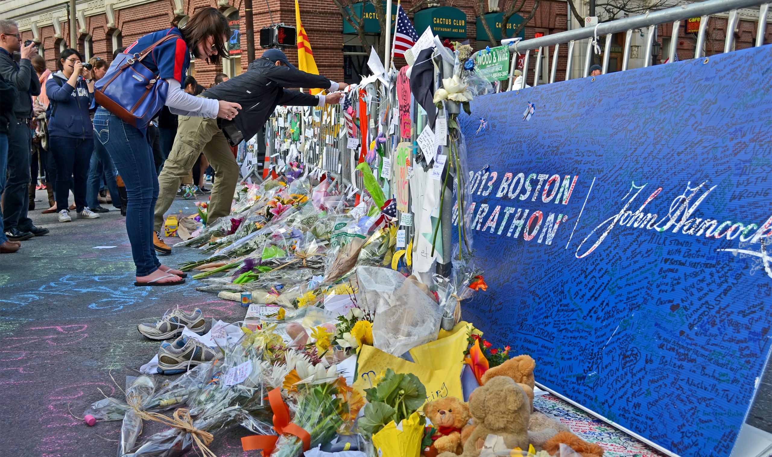woman leaning over a street memorial of flowers, cards, and tennis shoes for the Boston Marathon bombing victims