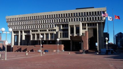 large concrete brutalist building with empty plaza and three flags in front