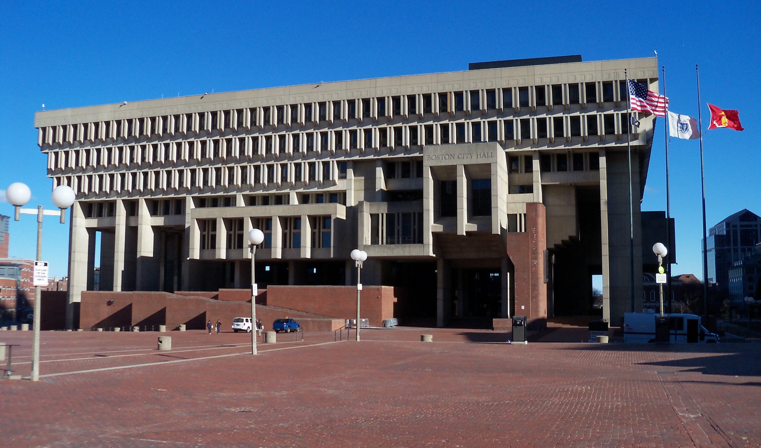 large concrete brutalist building with empty plaza and three flags in front