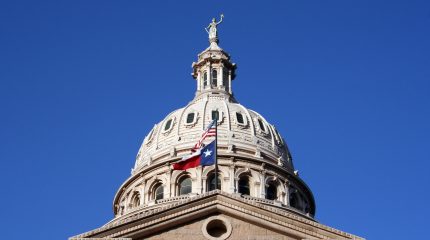 Texas and U.S. flags flying at the Texas State Capitol building
