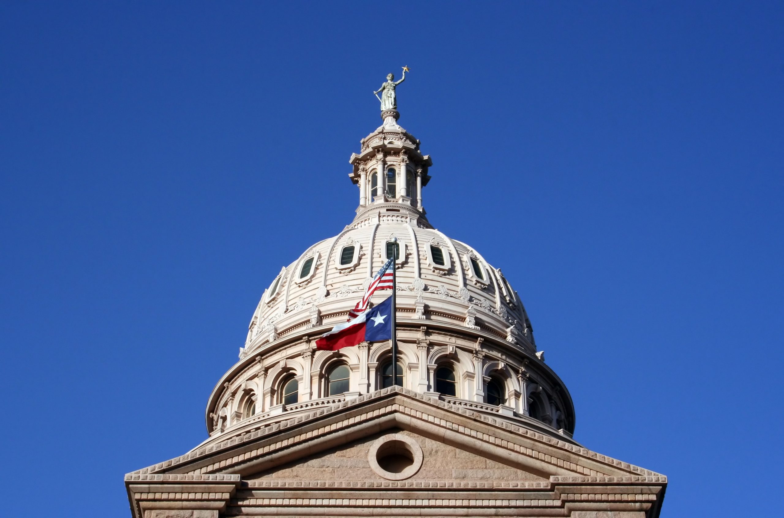 Texas and U.S. flags flying at the Texas State Capitol building