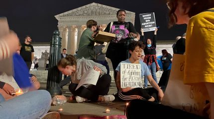 nighttime scene of people seated on ground with candles in front of supreme court
