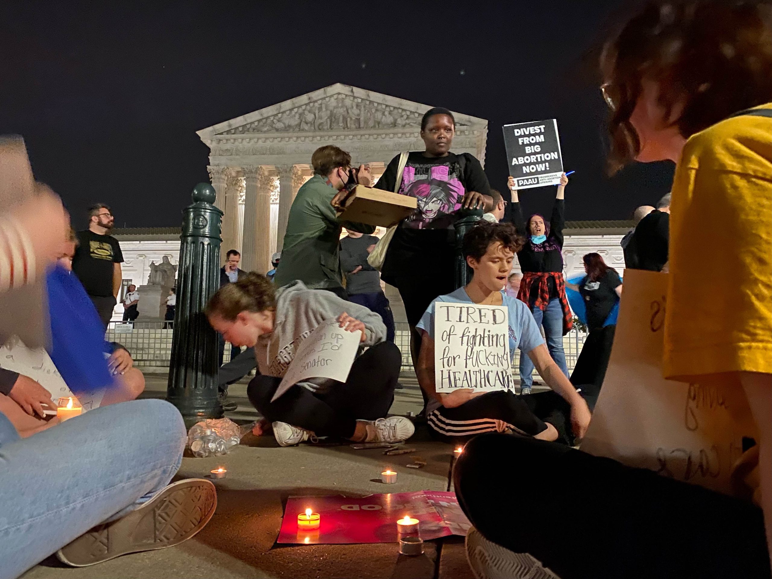 nighttime scene of people seated on ground with candles in front of supreme court