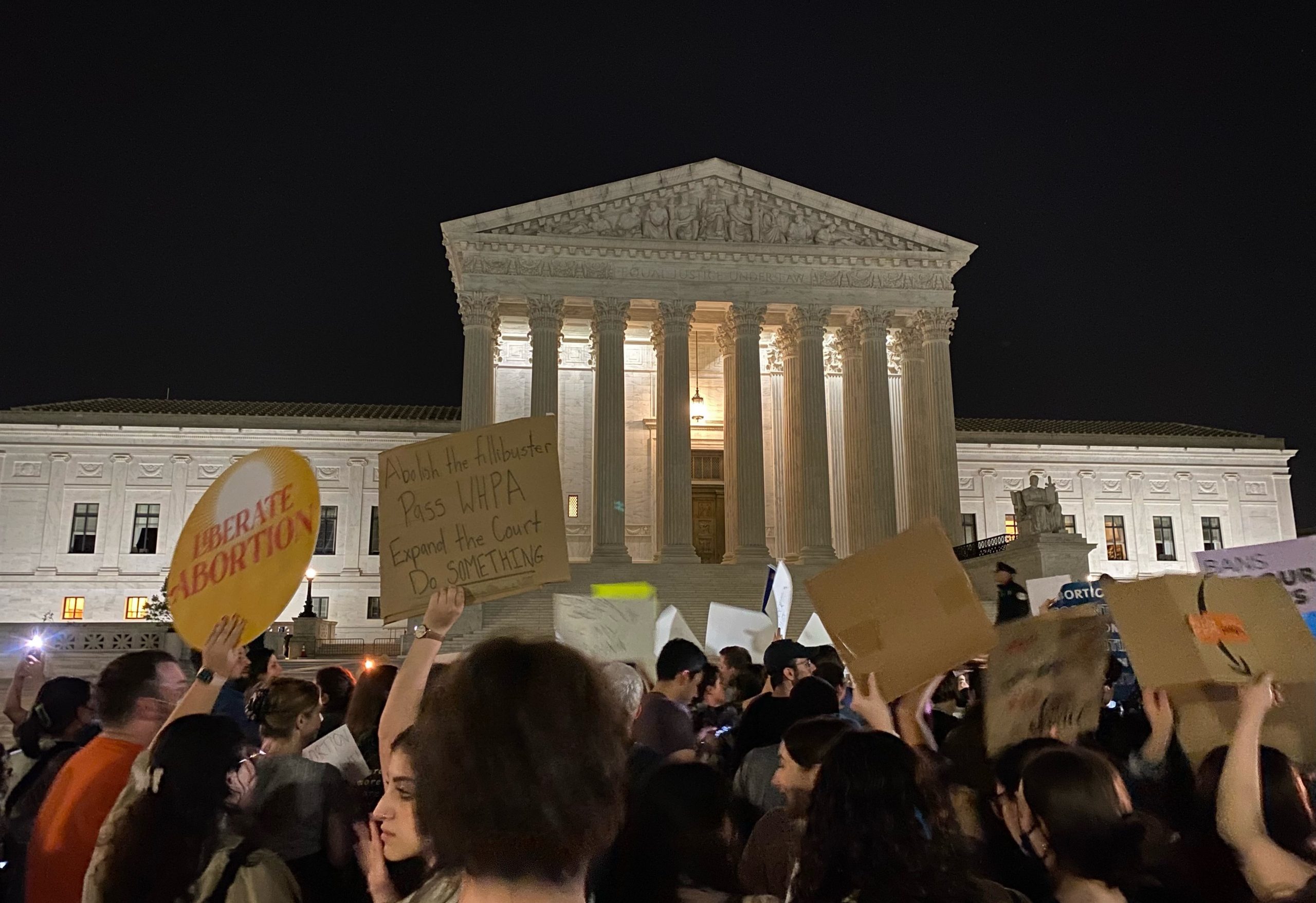 nighttime scene in front of supreme court, with crowd of people holding signs supporting abortion rights
