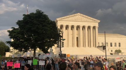 crowd of people stand in front of supreme court holding signs supporting abortion rights