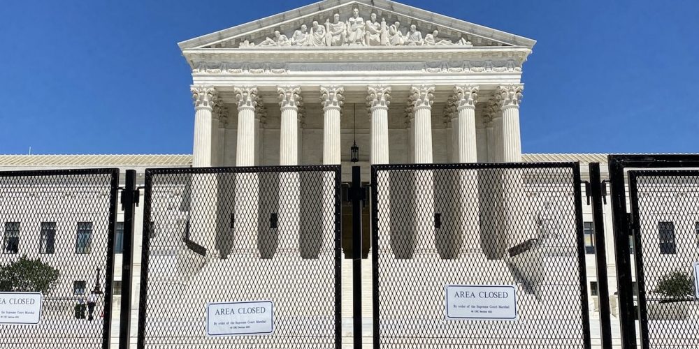 front facade of supreme court building with tall chain fence and "area closed" signs in foreground