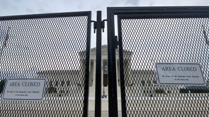 close up photo of chain-link security fence with front of supreme court building visible in background through the fence