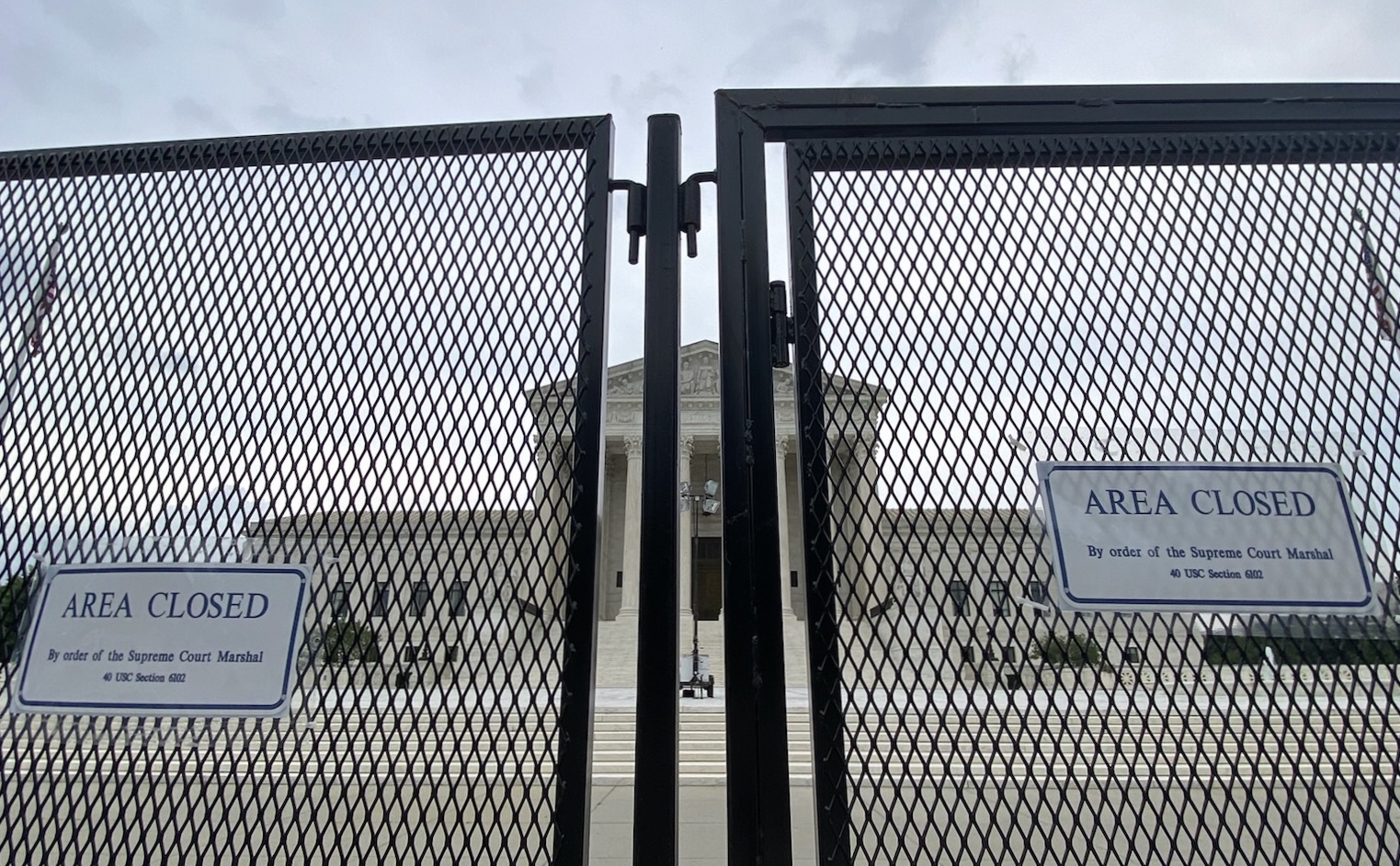 close up photo of chain-link security fence with front of supreme court building visible in background through the fence