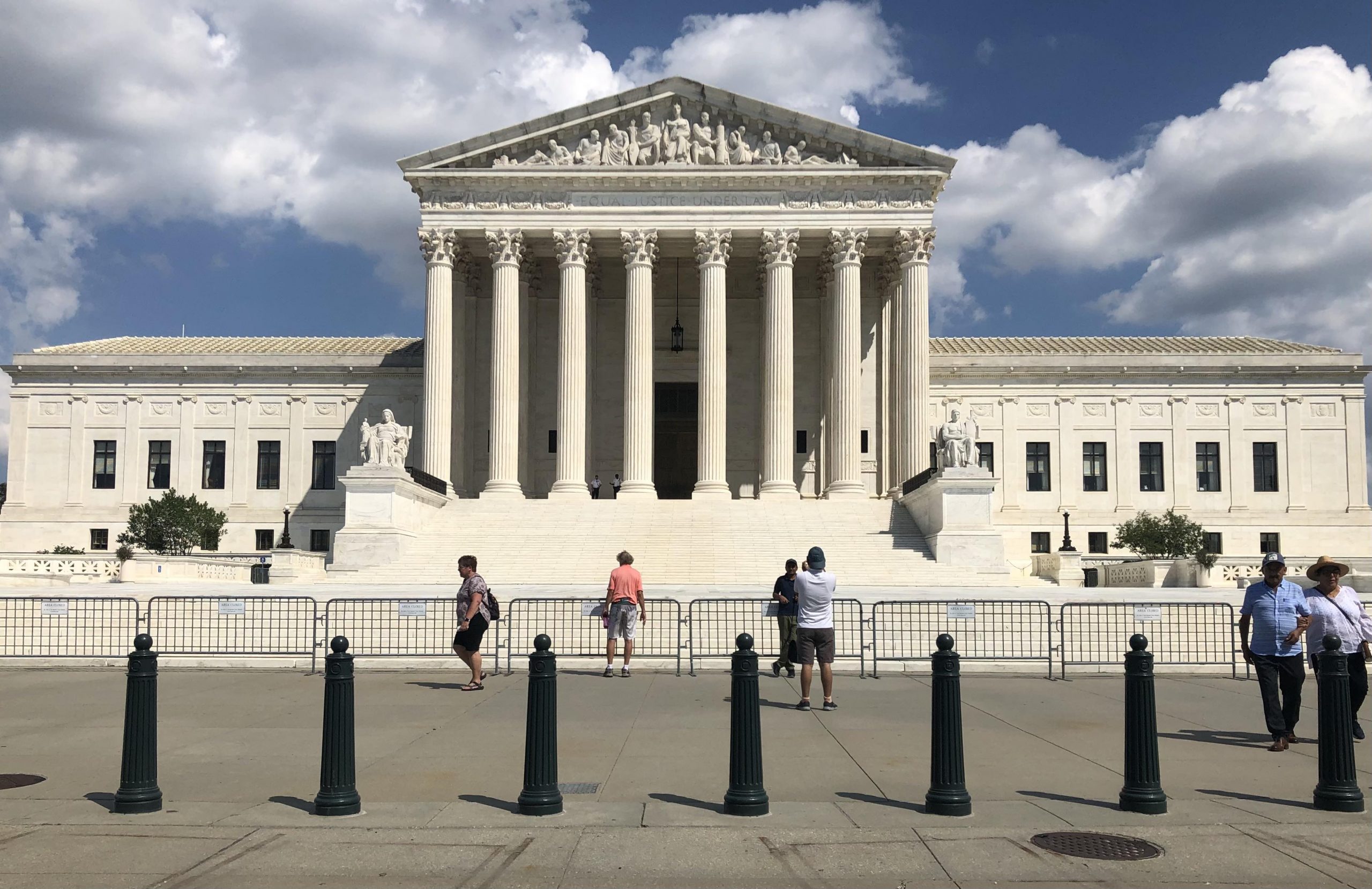 front view of supreme court showing pedestrians occupying sidewalk, with small metal barrier lining steps leading up to the plaza