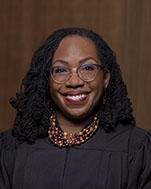headshot of Ketanji Brown Jackson smiling at camera. she wears a black judicial robe and colorful necklace.