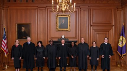 nine justices standing side by side, wearing black judicial robes.