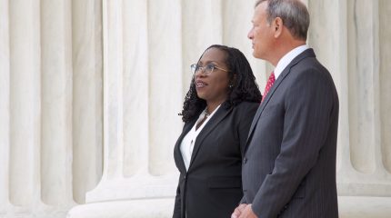 ketanji brown jackson and john roberts stand side by side with large marble columns in background