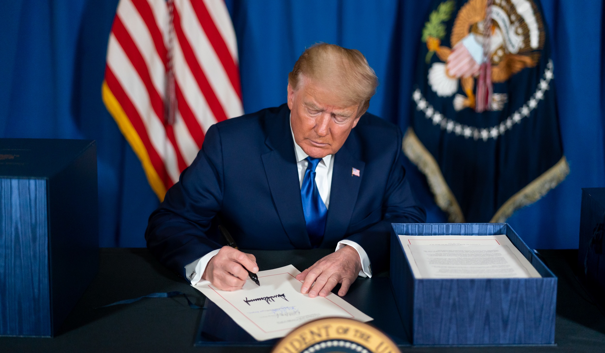 president trump sitting at desk and signing a document