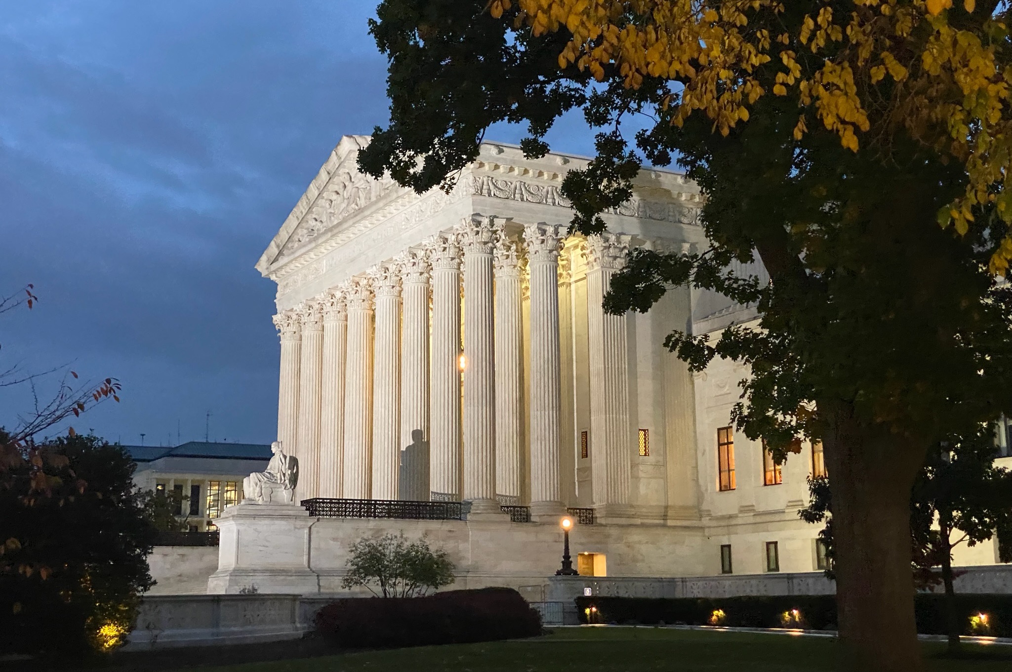 side view of supreme court building, illuminated against dark sky at dusk, with large tree in foreground