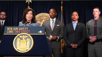 Woman speaking at podium with four people standing behind her.