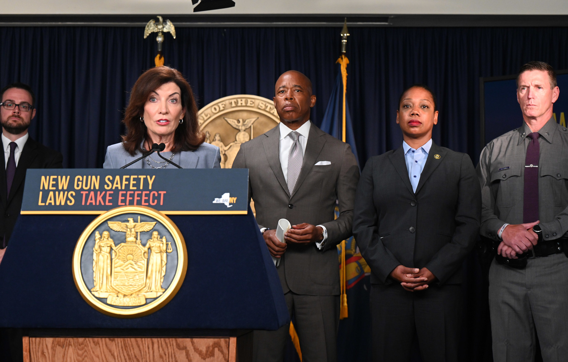 Woman speaking at podium with four people standing behind her.