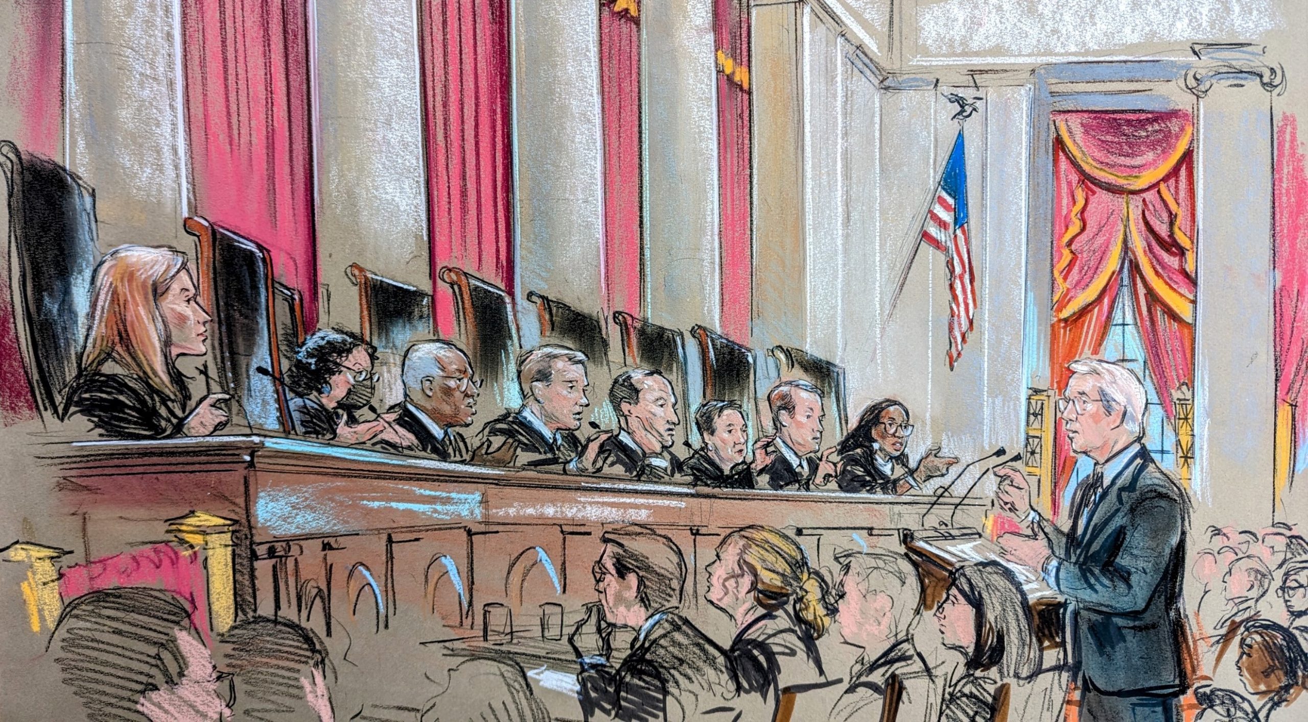 A man speaks at a lecture before nine justices on the bench who all seem to be asking him a question.