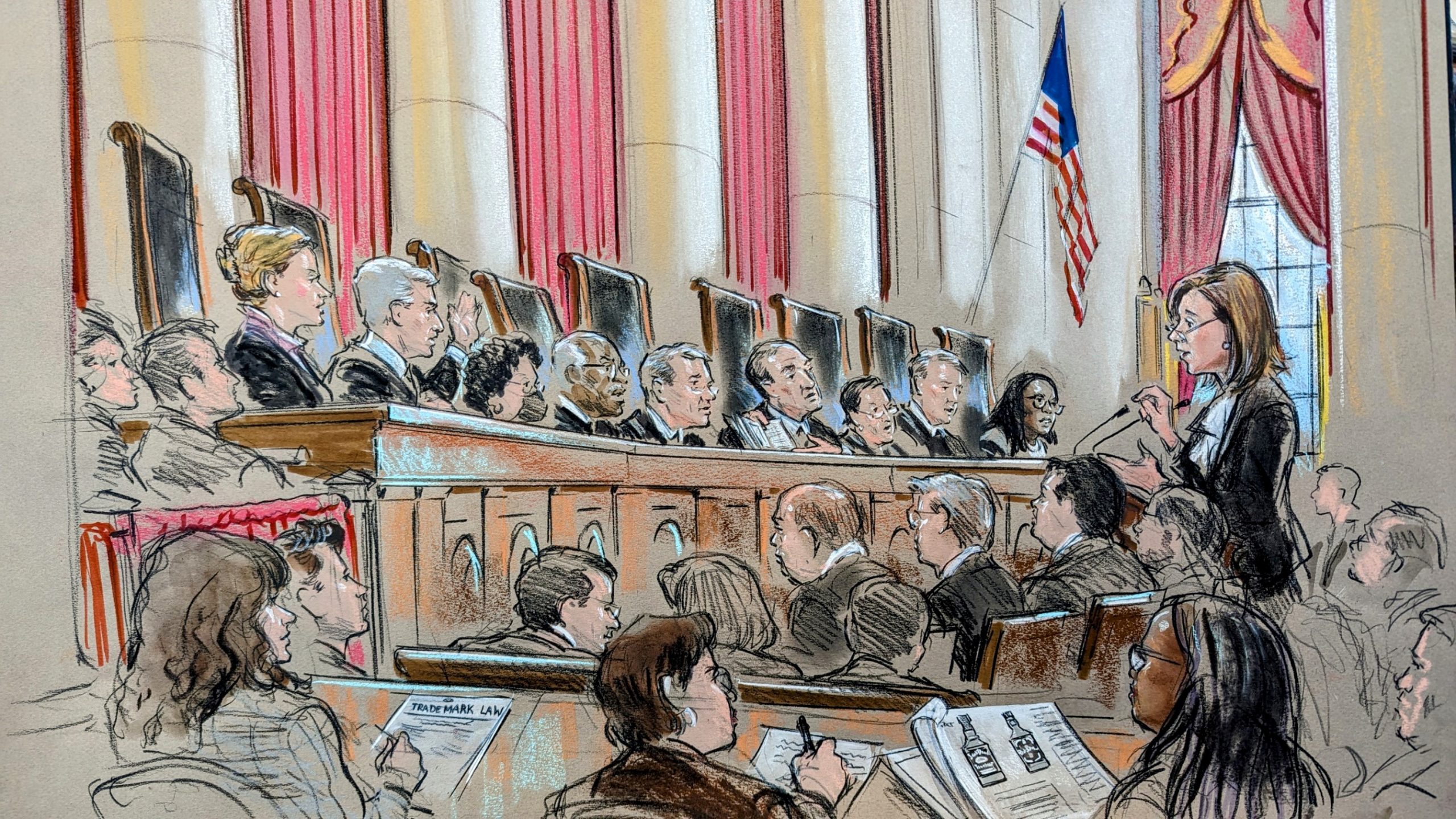 Sketch of the courtroom as a woman argues before the podium. Audience and several reporters can be seen, in addition to the full podium. Justice Gorsuch raises his hand while Justice Alito holds up and gestures to some documents.