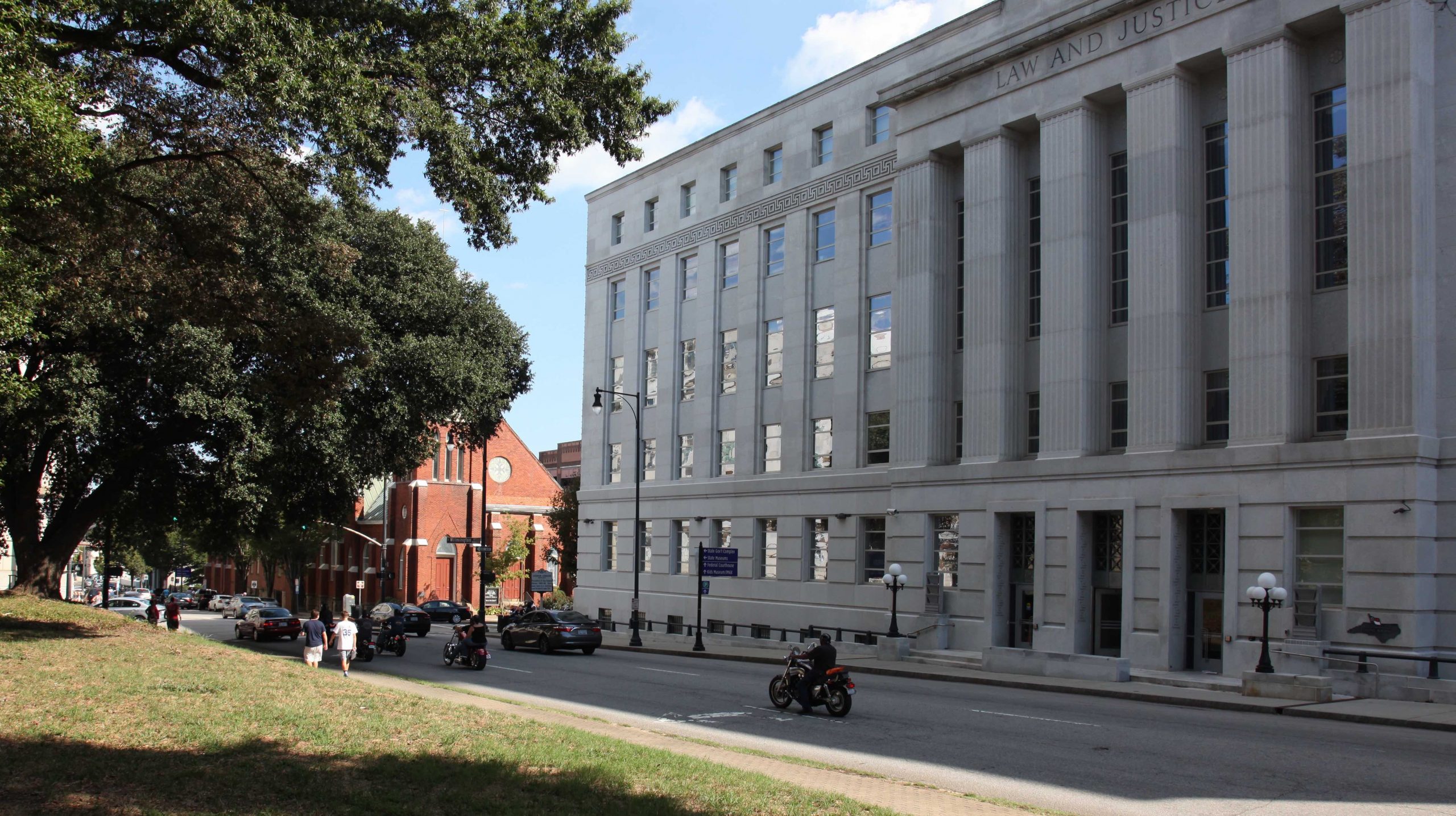 A large grey building with "Law and Justice" carved into the stone at the top, across the street is a grassy park.