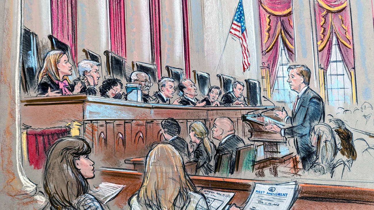 Man at lectern as audience and justices listen in.