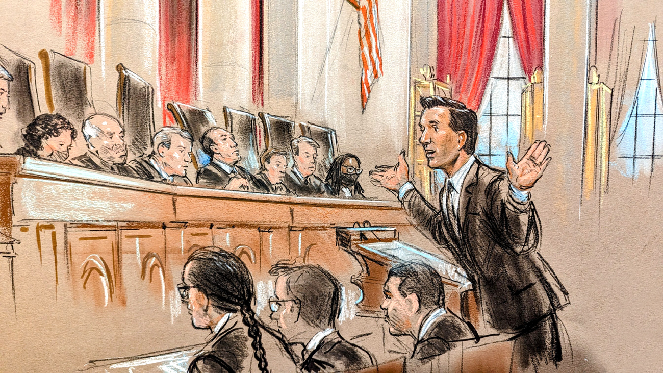 Man speaking with hands raised in front of nine justices on the bench