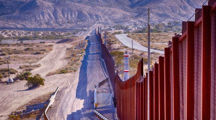 Border fence cutting through a desert with hills in the background