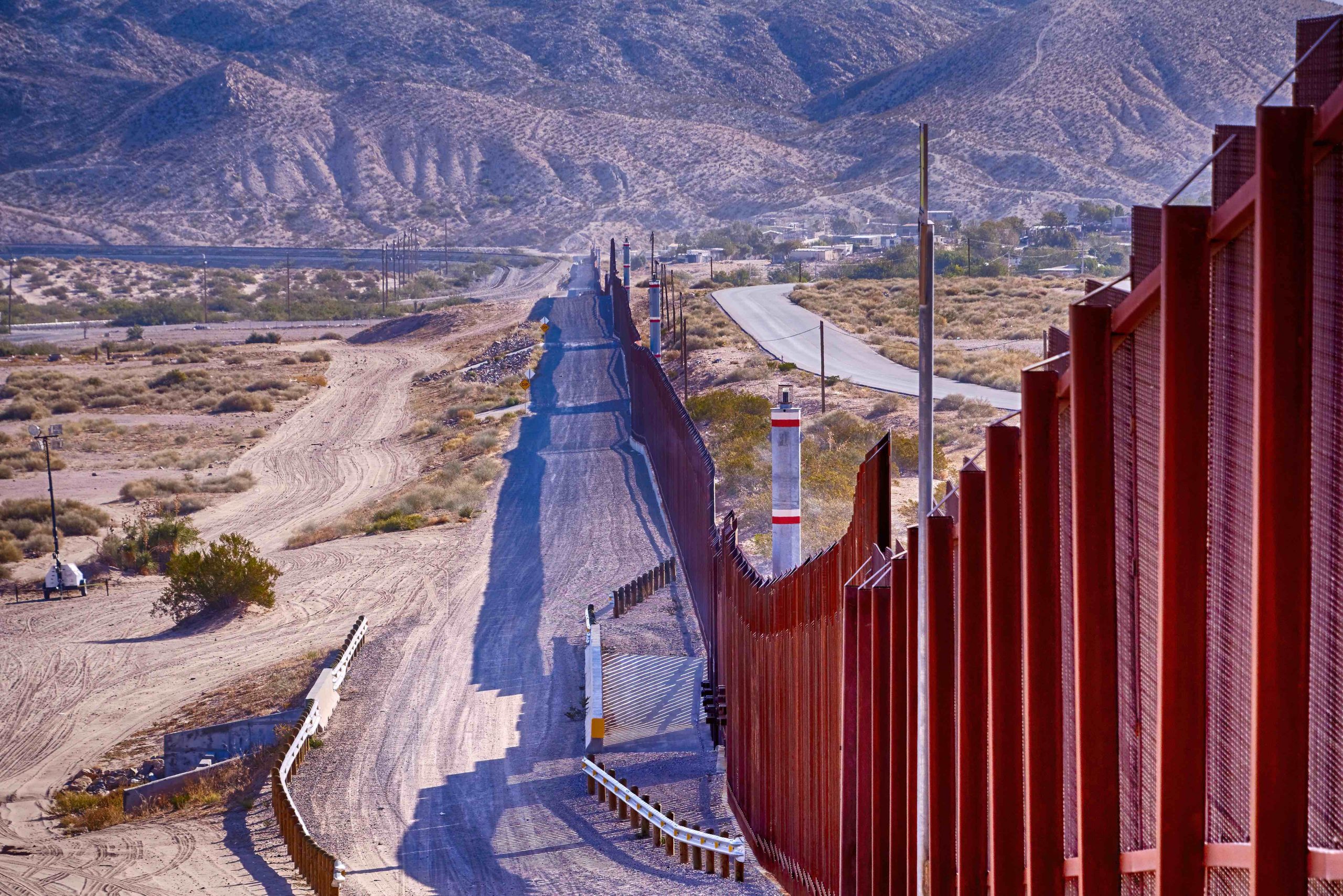 Border fence cutting through a desert with hills in the background