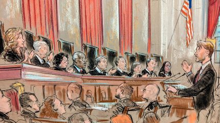 All nine justices speaking on the bench to lawyer at lectern with group looking on.